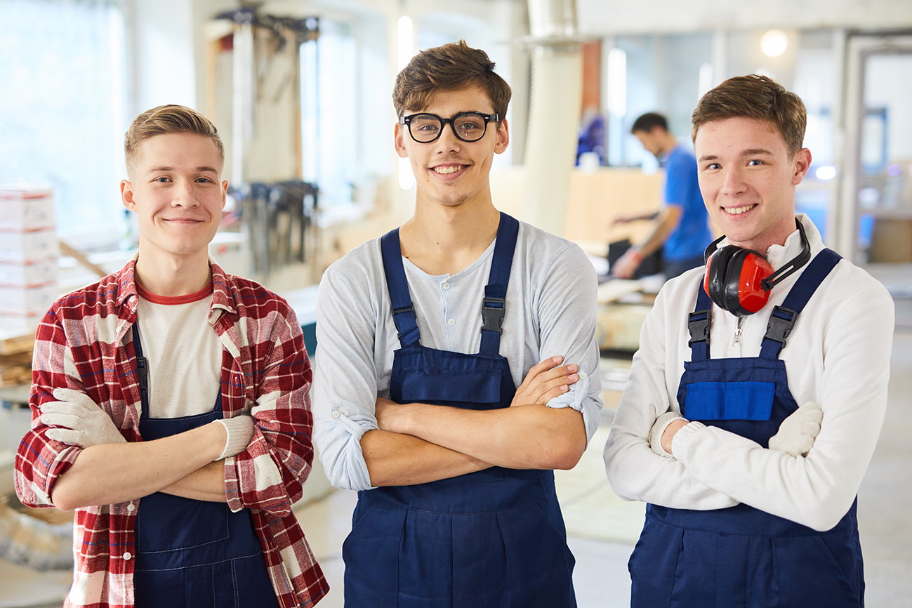 three carpentry students smiling at work posing with crossed arms