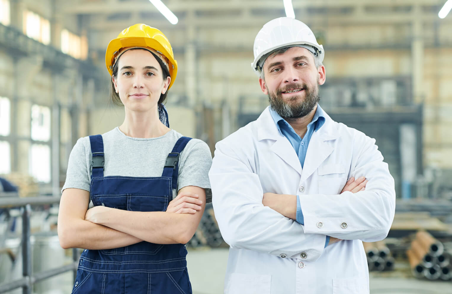 two confident workers standing inside a warehouse wearing construction helmets